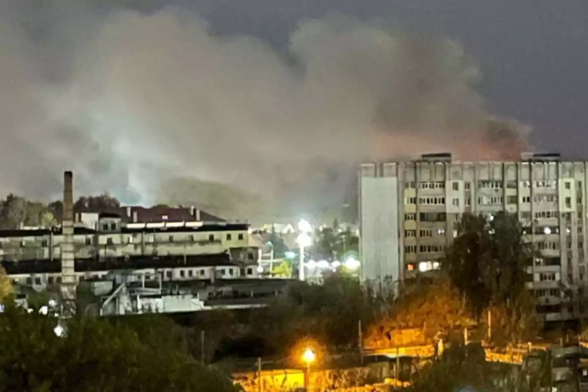 Edificios urbanos con humo denso en el cielo durante la noche.