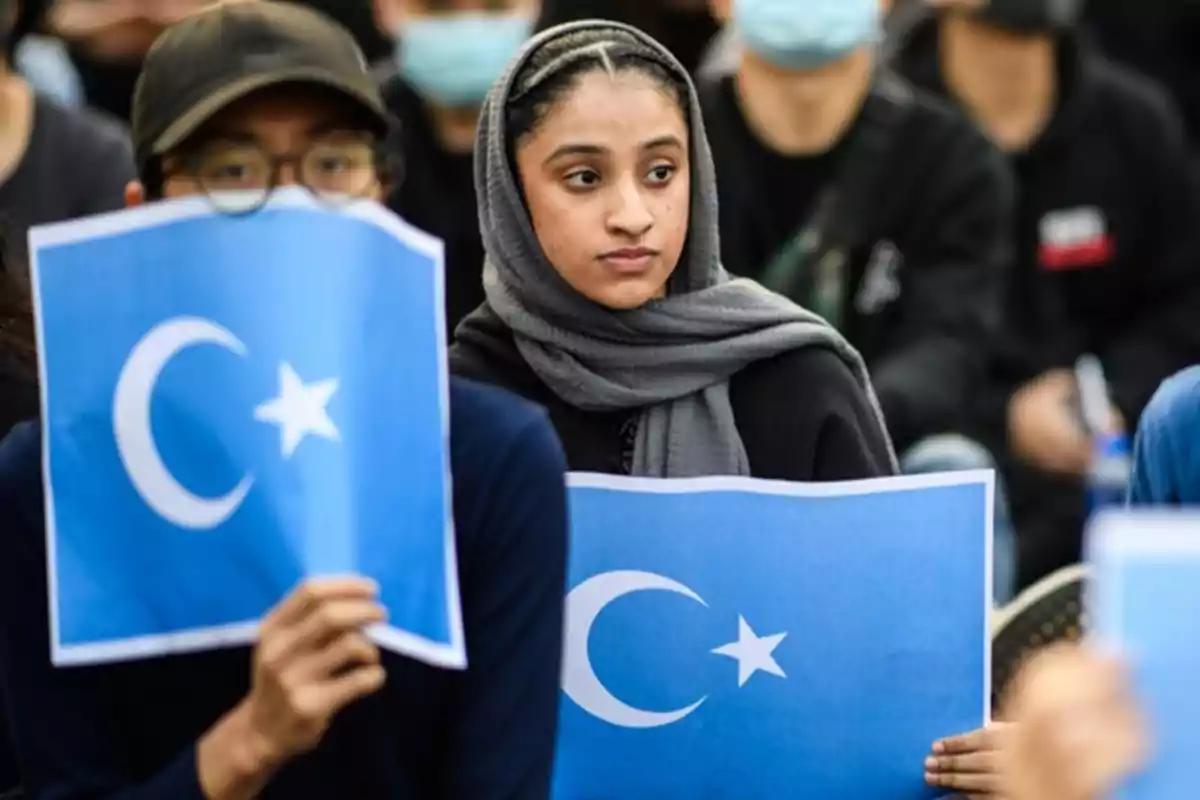 Personas sosteniendo carteles con la bandera de la región de Xinjiang en una manifestación.