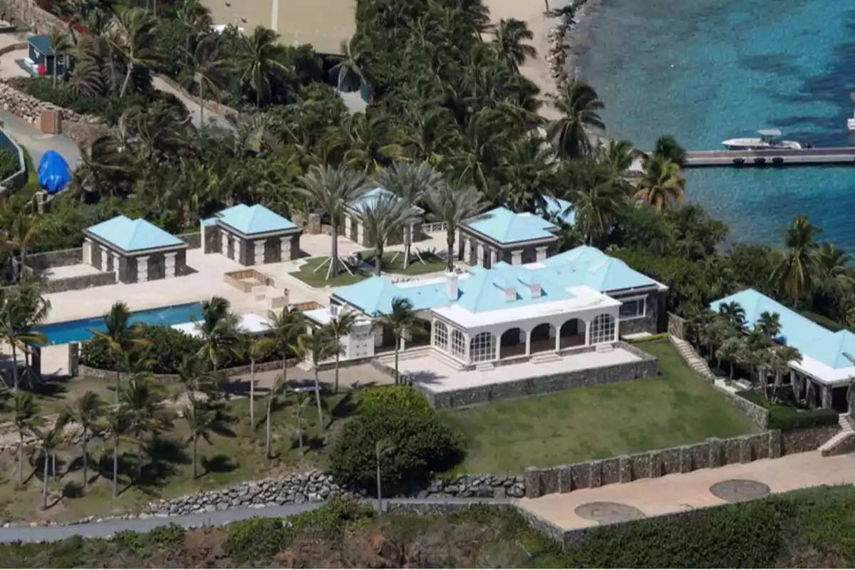 Una lujosa villa con techos azules rodeada de palmeras y ubicada junto a un mar de aguas cristalinas.