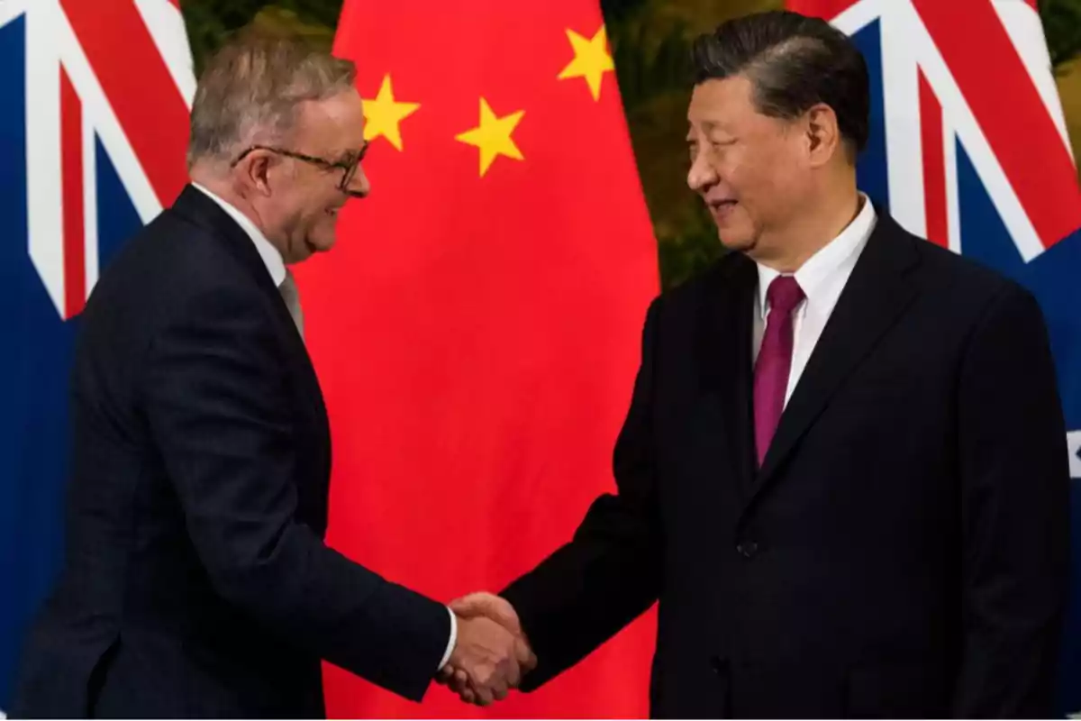 Dos personas dándose la mano frente a banderas de China y Australia.