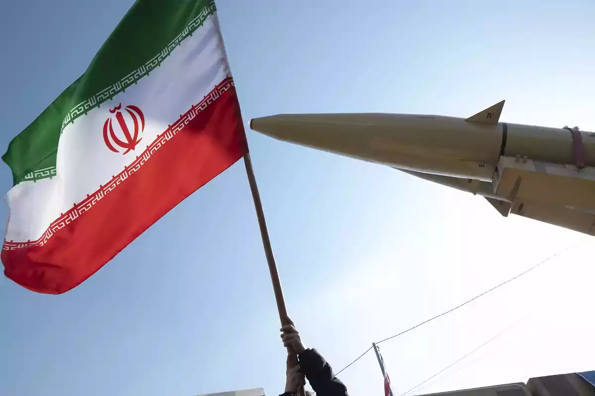 Bandera de Irán ondeando junto a un misil apuntando hacia el cielo.