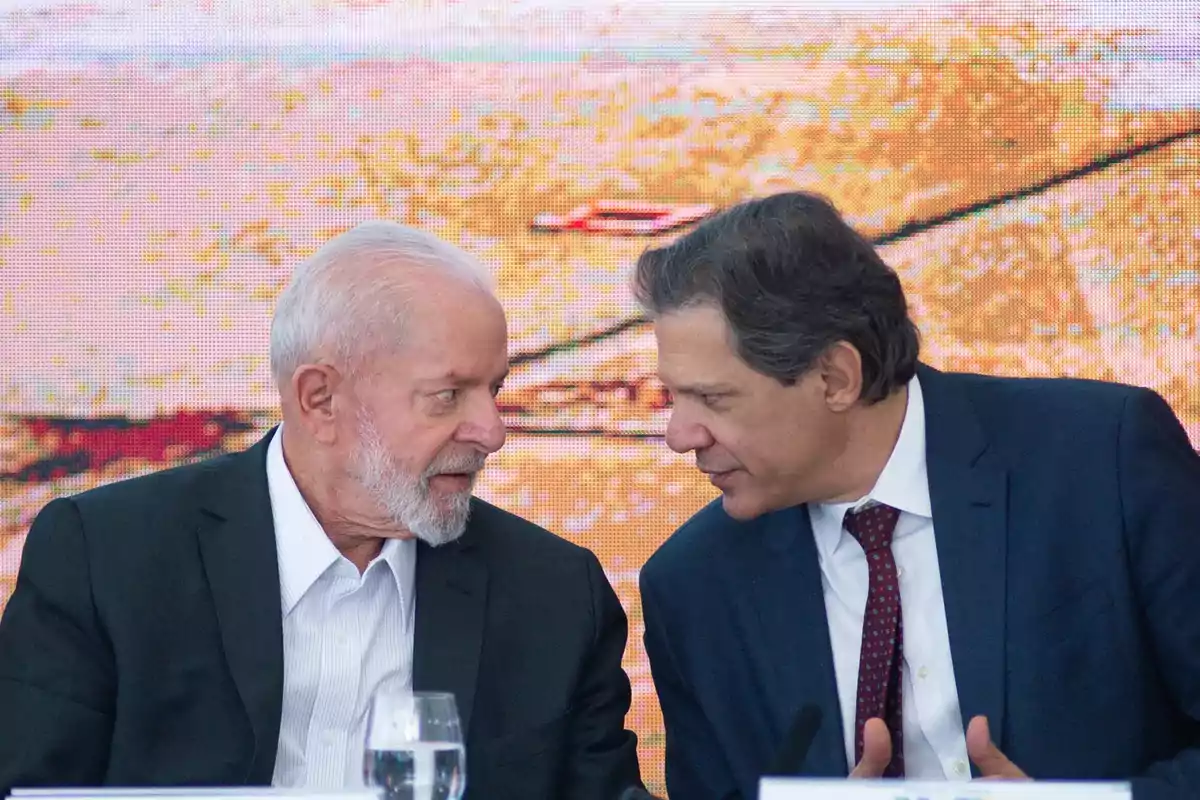 Dos hombres conversando en un evento formal con fondo colorido.