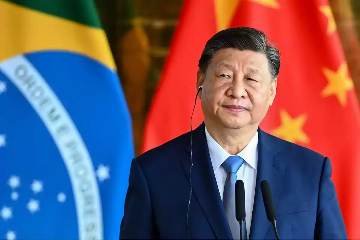 Un hombre en traje azul con auriculares frente a las banderas de Brasil y China.