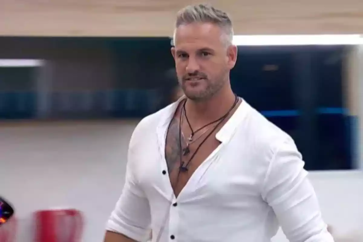 Man with a white jersey and necklaces in a modern interior.