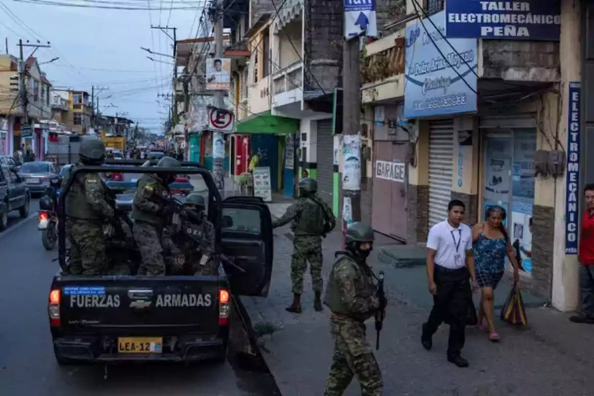 Soldados armados patrullan una calle concurrida desde la parte trasera de un vehículo militar mientras peatones caminan por la acera.