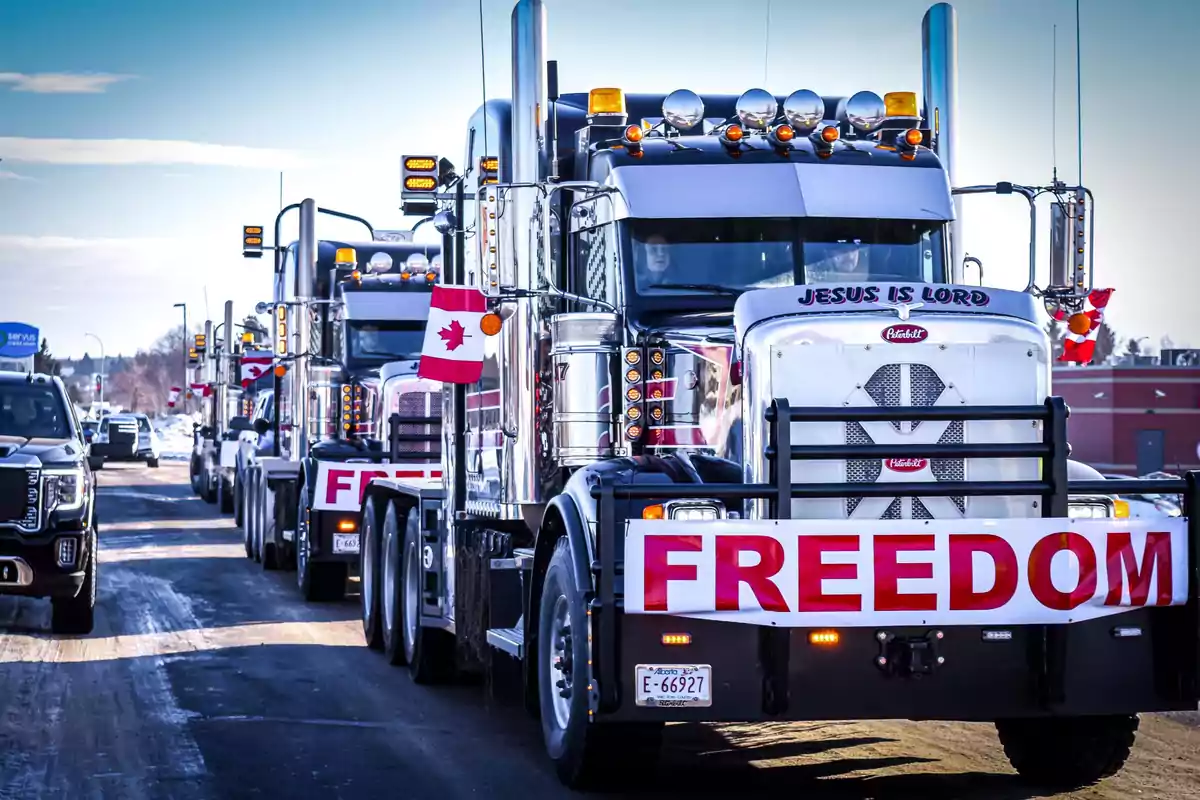 Una fila de camiones grandes con banderas de Canadá y pancartas que dicen "FREEDOM" en una carretera nevada.