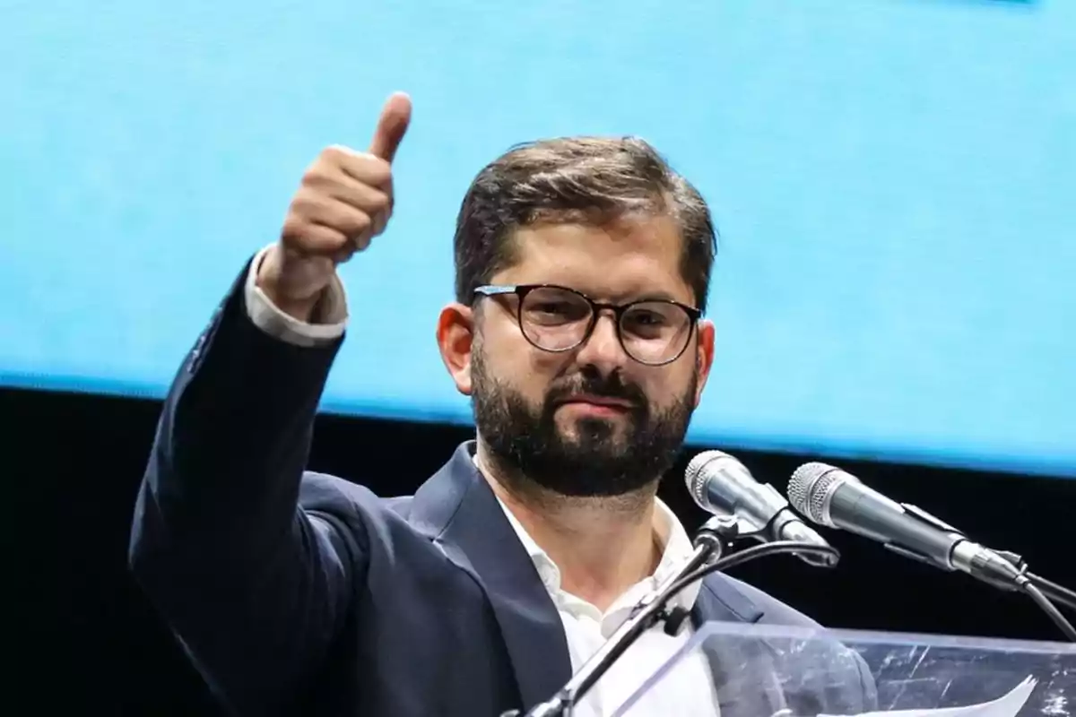 Un hombre con gafas y barba levanta el pulgar mientras habla en un micrófono.