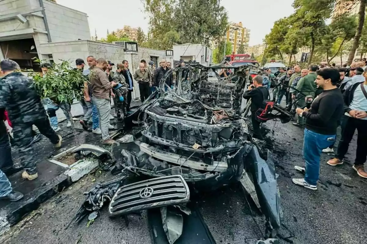 Un grupo de personas observa los restos de un vehículo destruido en una calle.