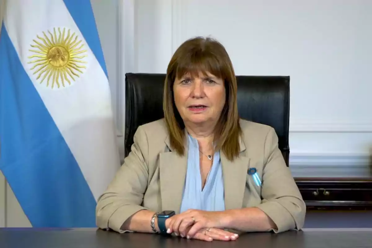 Una mujer sentada en un escritorio con una bandera argentina al fondo.