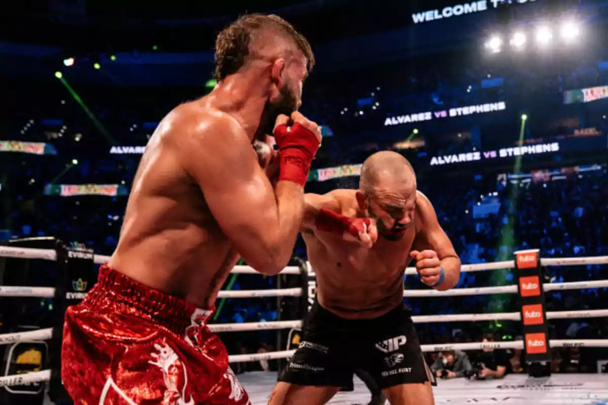 Dos boxeadores intercambian golpes en un ring iluminado durante un combate con público en el fondo.