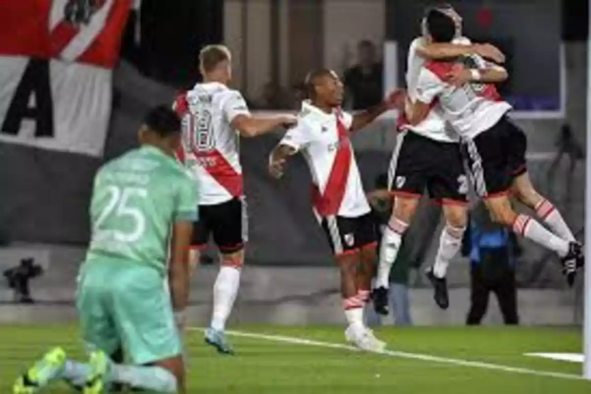 Jugadores de fútbol celebrando un gol en el campo mientras un jugador del equipo contrario está arrodillado.