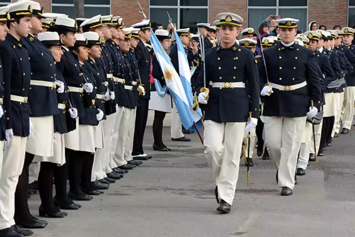 Cadetes de una academia militar marchando en formación con uniformes formales y banderas argentinas.