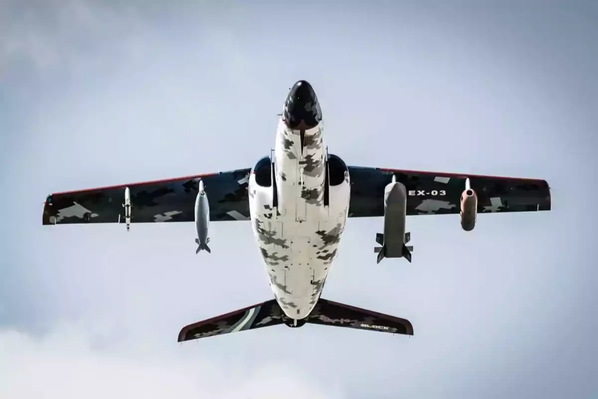 Vista inferior de un avión militar con camuflaje en vuelo mostrando su armamento.