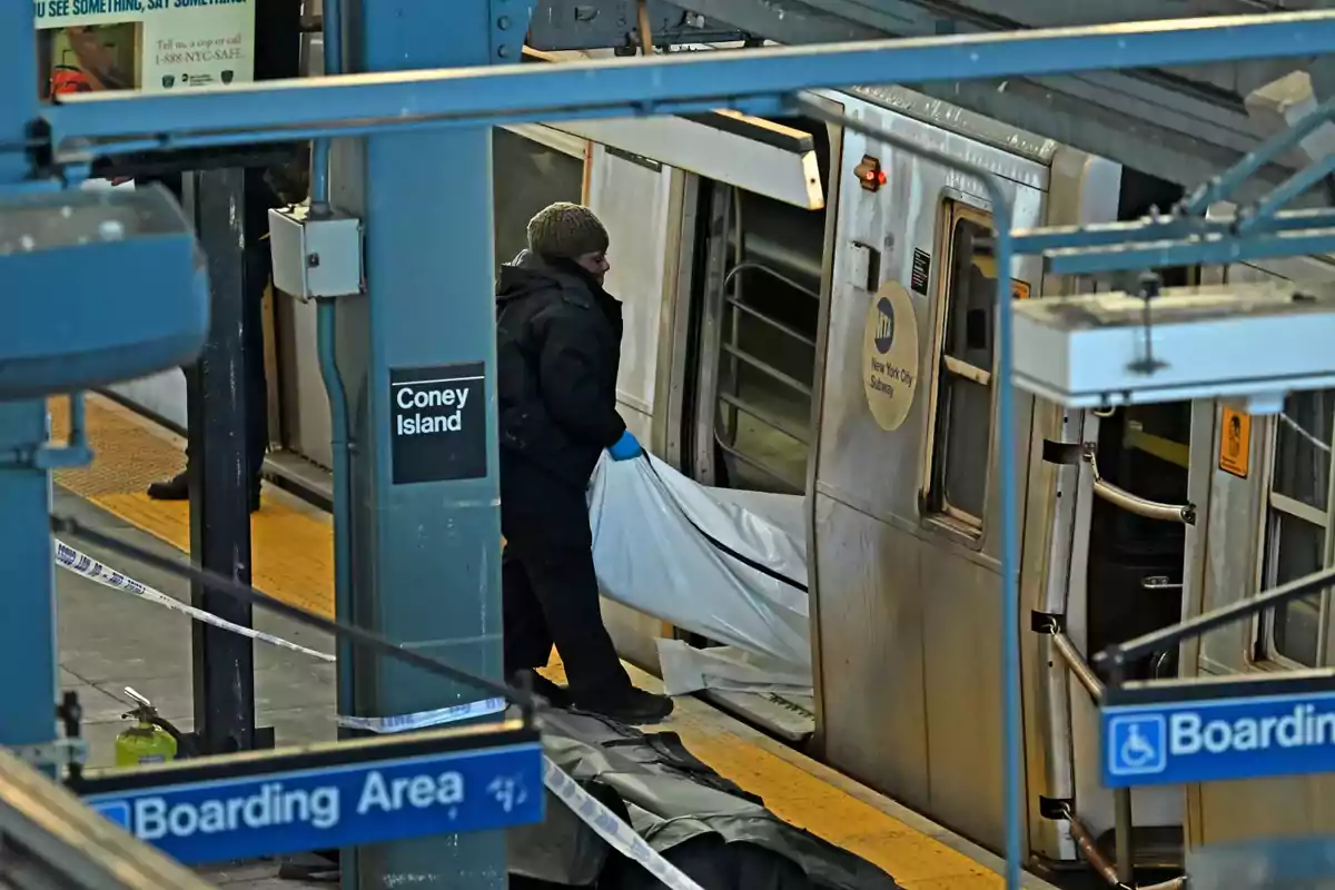 Una persona con guantes azules maneja una bolsa blanca cerca de un vagón del metro en la estación de Coney Island.