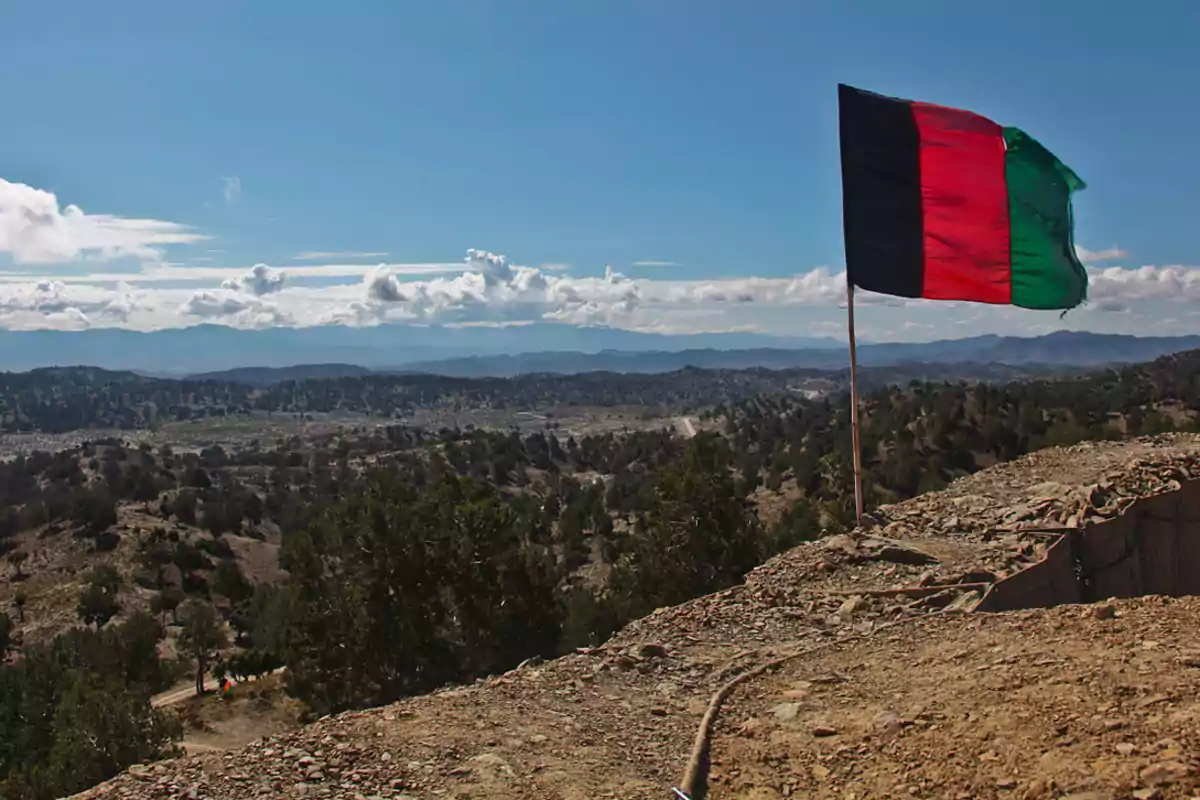 Una bandera ondea en un paisaje montañoso con cielo despejado y nubes esponjosas.