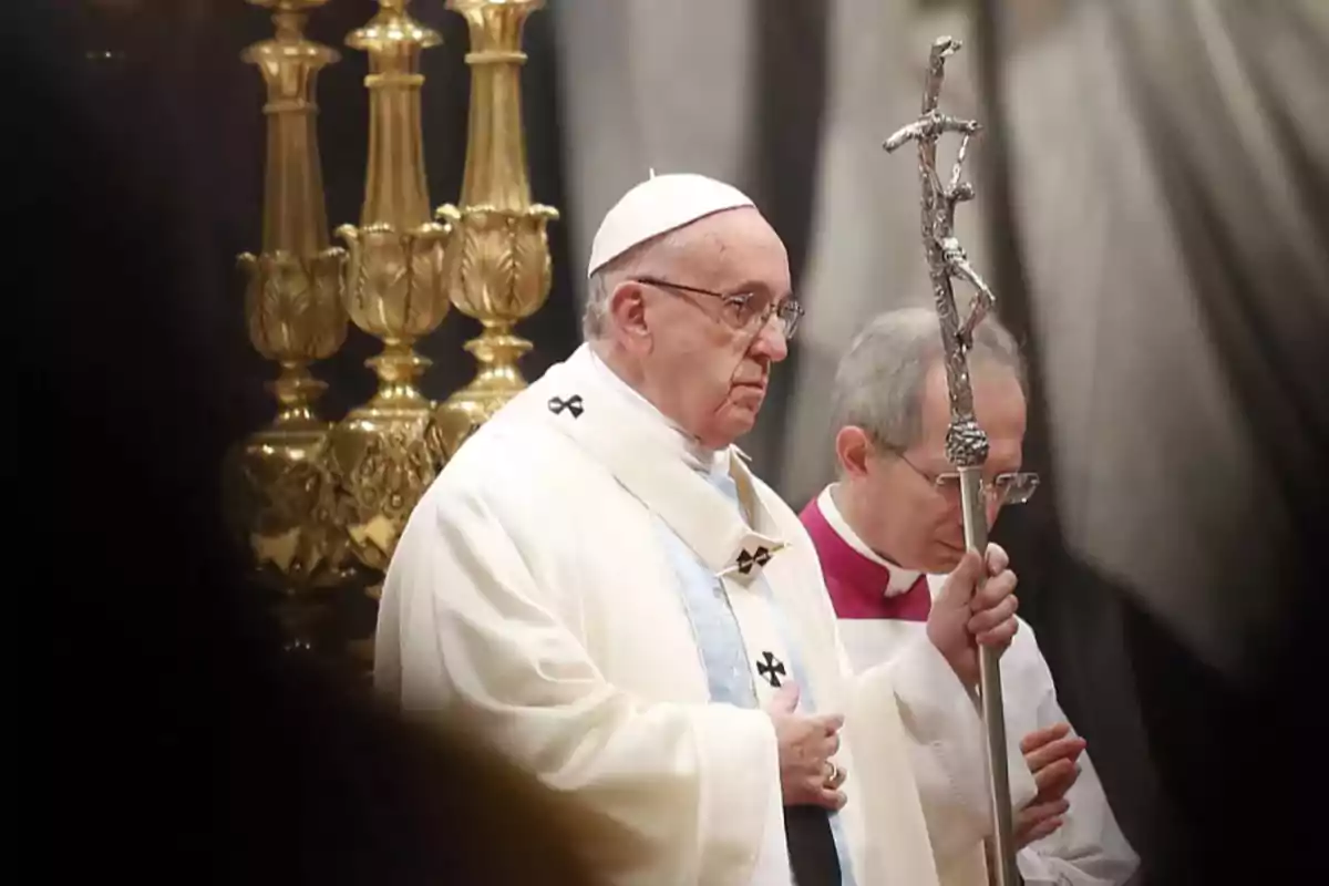 Un líder religioso vestido con vestimenta ceremonial blanca sostiene un báculo en un entorno eclesiástico.