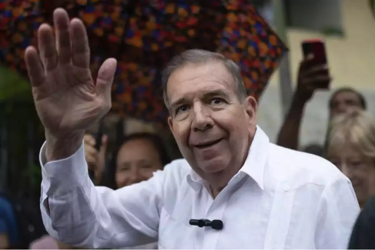 Hombre mayor saludando con la mano en un evento al aire libre.