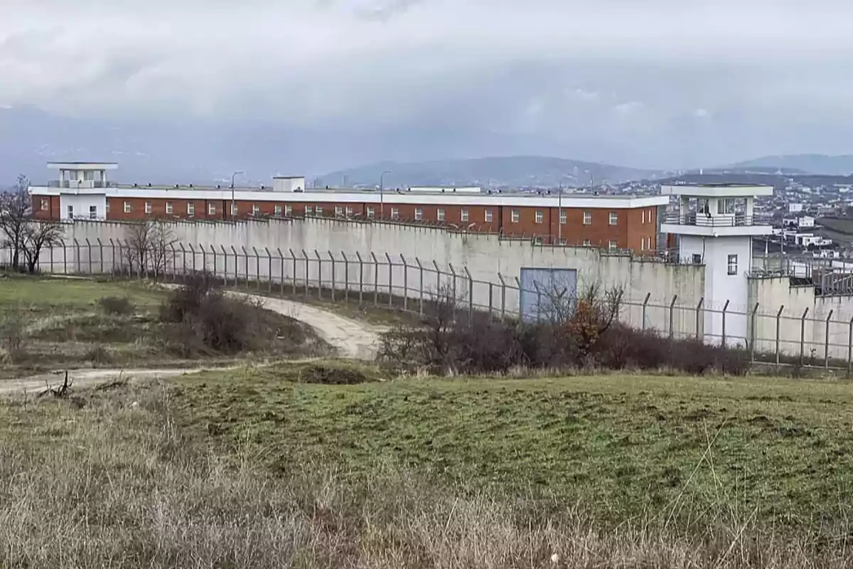 Vista de una prisión con muros altos y torres de vigilancia en un entorno rural.