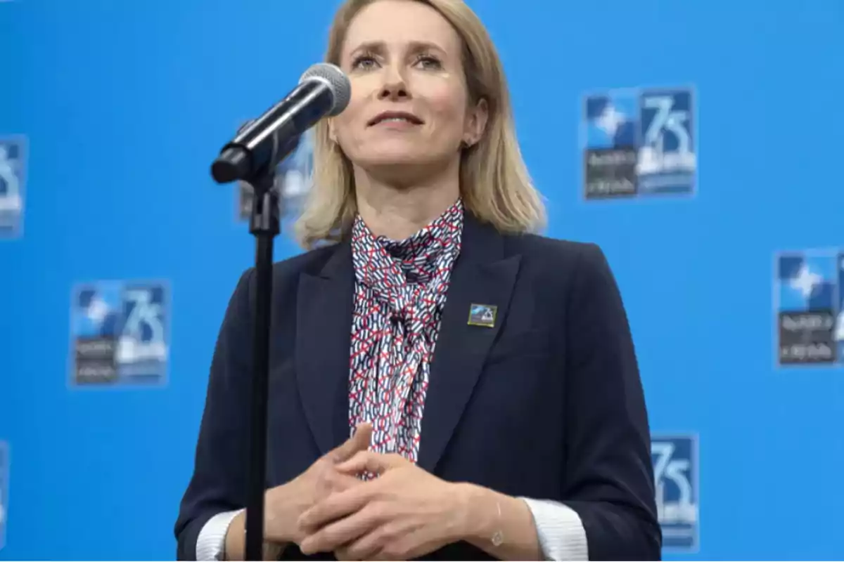 Mujer hablando frente a un micrófono con fondo azul y logotipos.