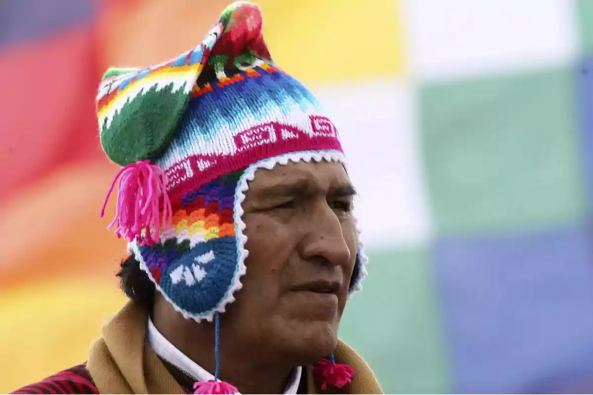 Un hombre con un colorido gorro andino de lana con borlas rosas y un fondo de colores.