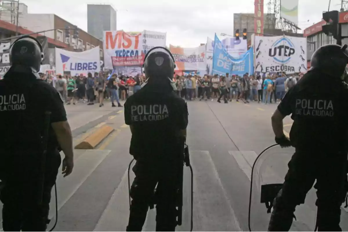 Policías de la ciudad con equipo antidisturbios observan una manifestación con pancartas en una calle.