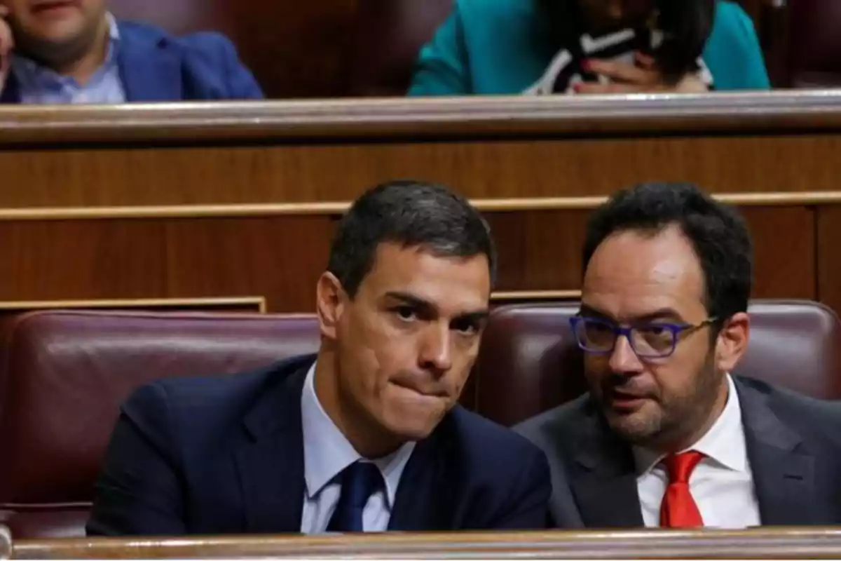 Dos hombres en traje conversando en un entorno formal.