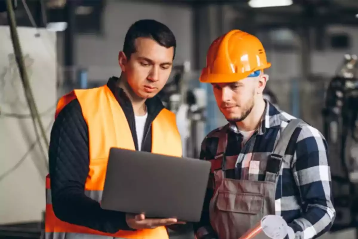 Dos trabajadores revisan información en una computadora portátil en un entorno industrial.