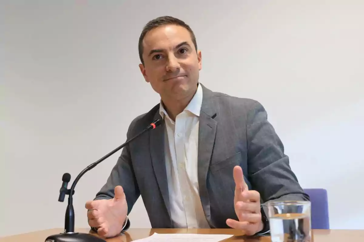 Hombre en traje gris hablando en un micrófono durante una conferencia de prensa.