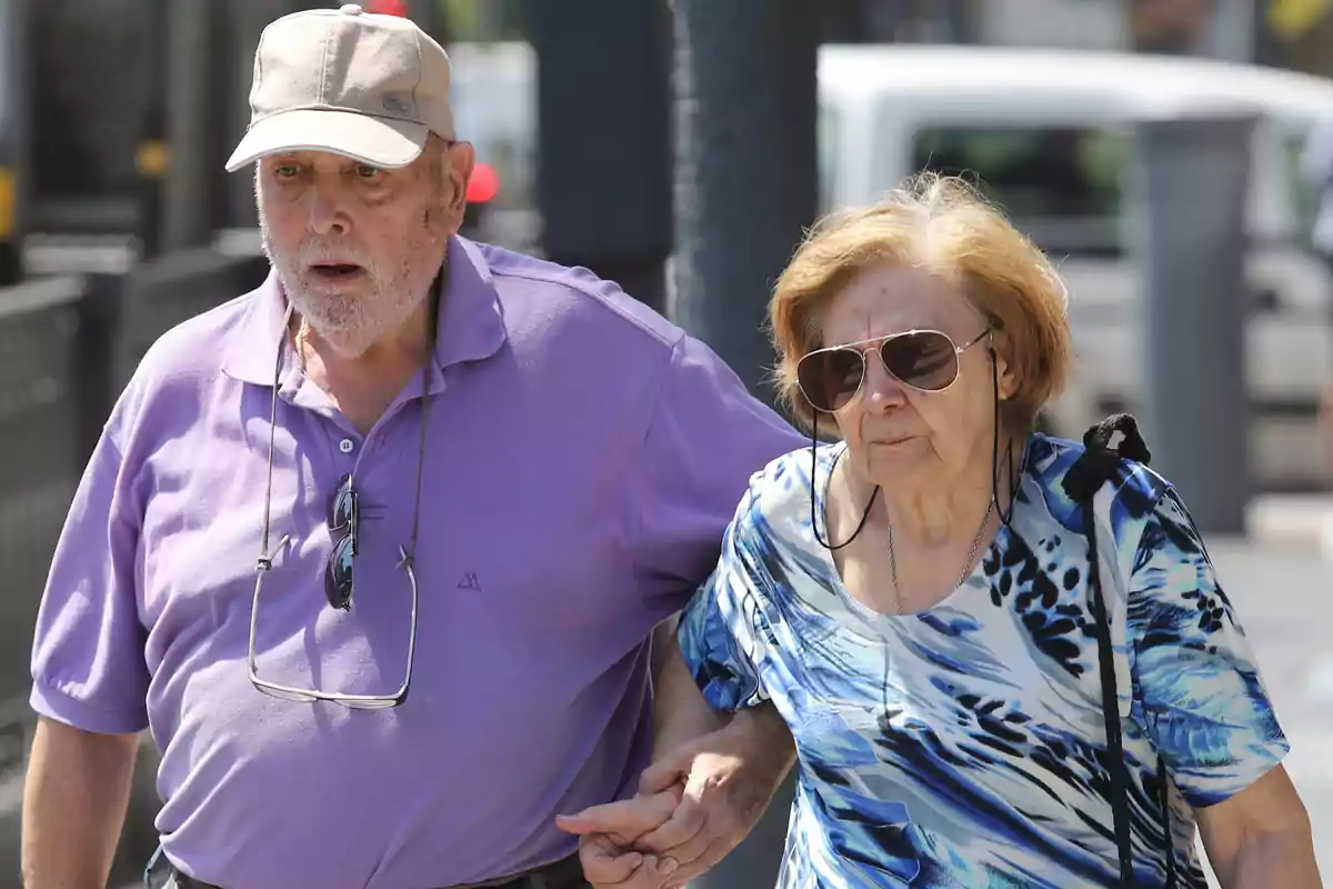 Una pareja de personas mayores caminando juntas de la mano en un entorno urbano.