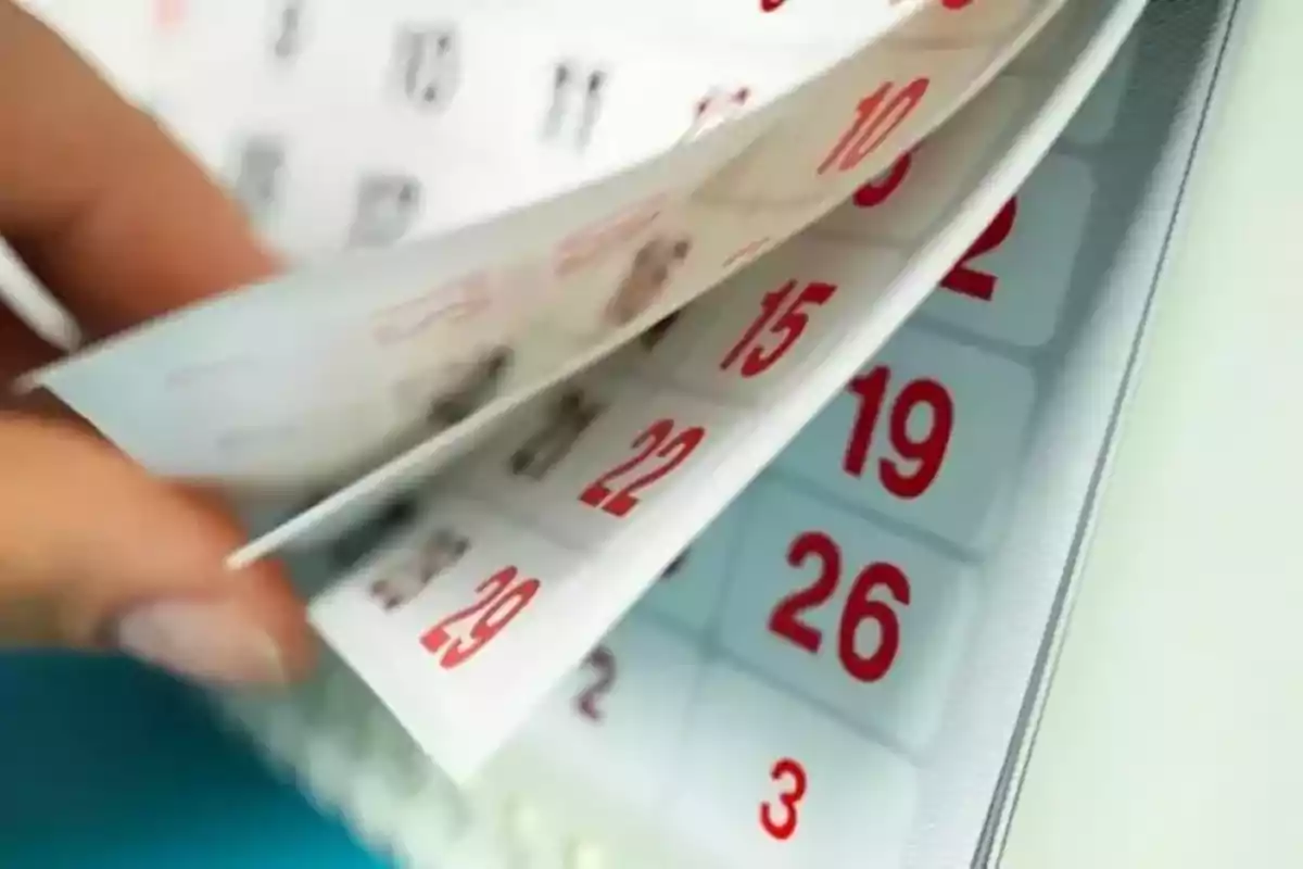 Una mano pasando las páginas de un calendario con números en rojo.