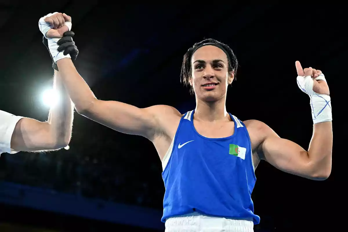 Un boxeador con uniforme azul levanta los brazos en señal de victoria mientras un árbitro sostiene su mano.