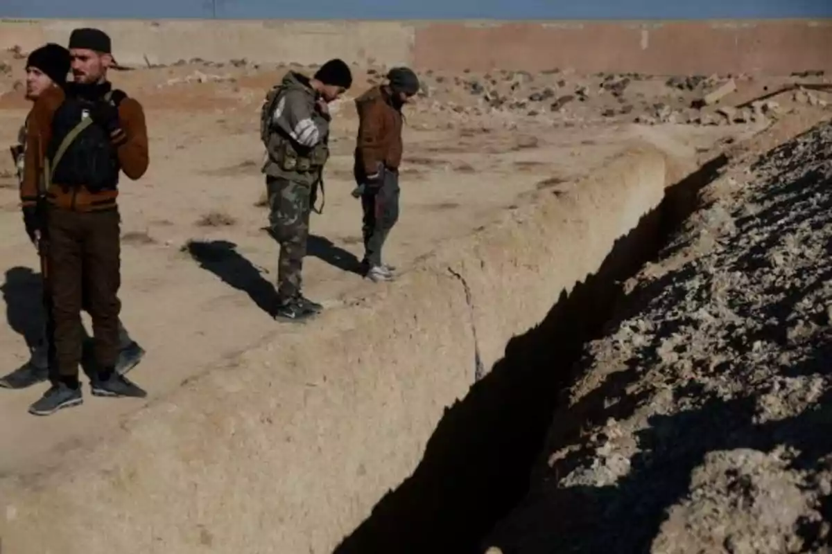 Un grupo de personas vestidas con ropa militar observa una zanja en un terreno árido.