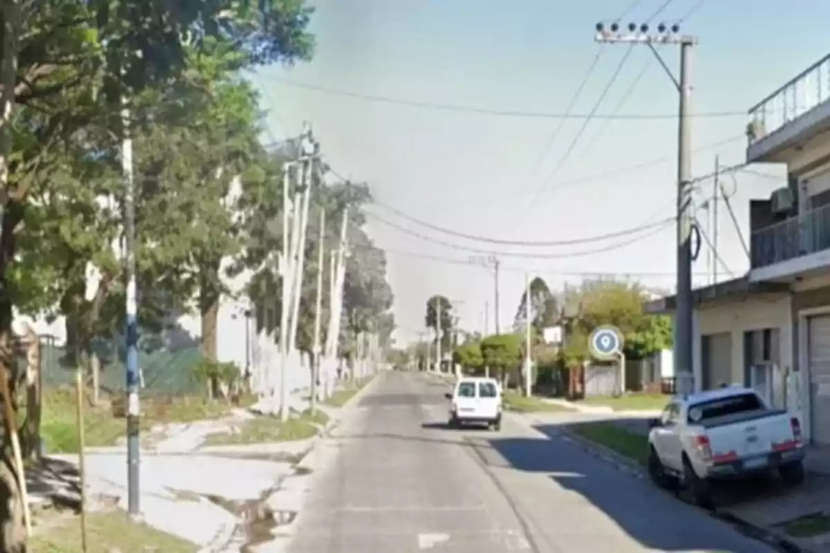 Una calle urbana con árboles a los lados, postes de luz y vehículos estacionados.