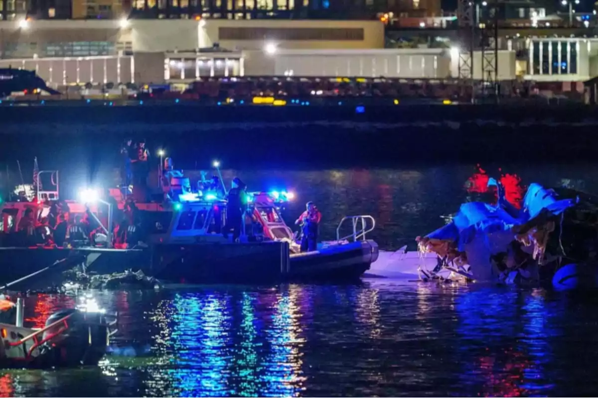 Barcos de rescate iluminados con luces azules y rojas junto a restos de un avión en el agua durante la noche.