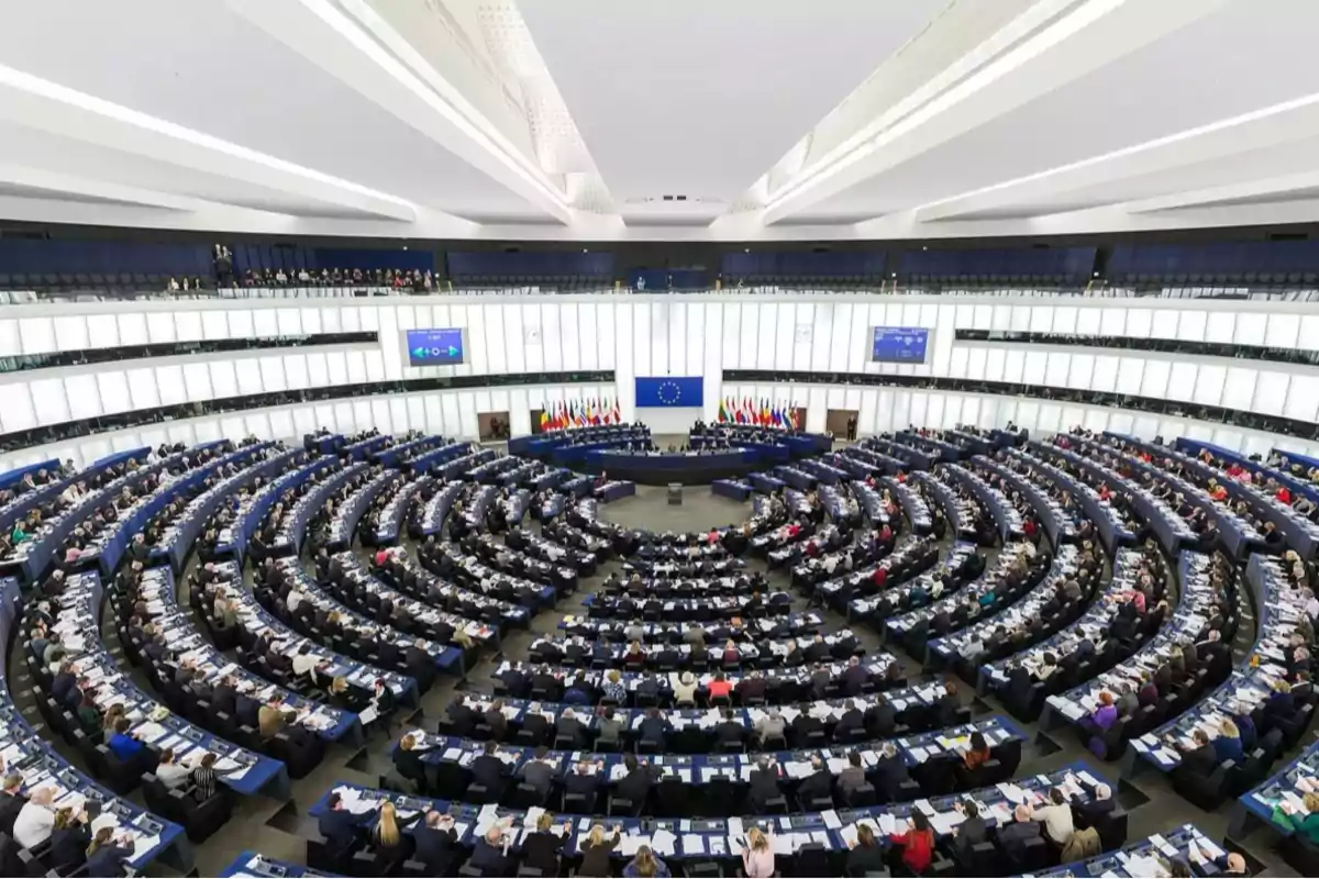 A panoramic view of the interior of a parliament with rows of seats arranged in a semicircle and a large number of people present.