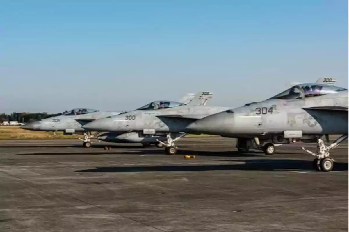 Tres aviones de combate estacionados en una pista de aterrizaje bajo un cielo despejado.