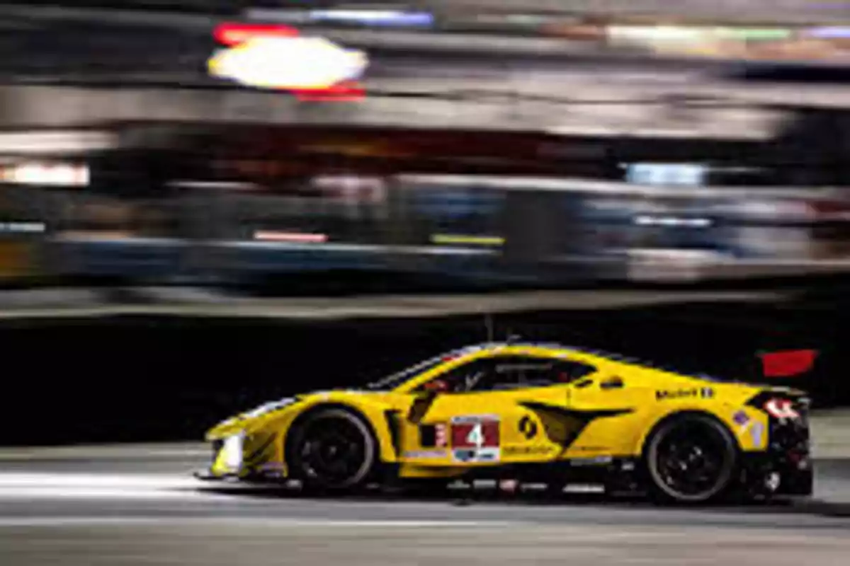 Un coche de carreras amarillo en movimiento en una pista iluminada por la noche.