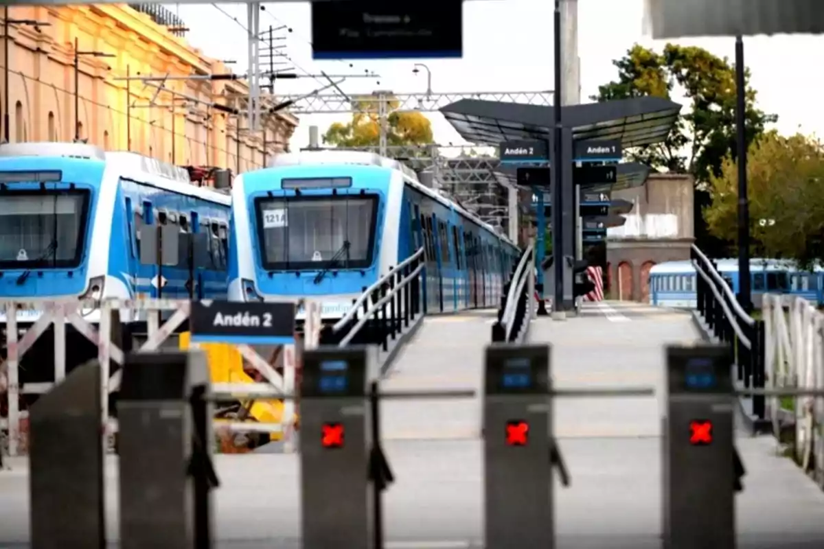 Trenes azules en una estación con andenes y torniquetes en primer plano.