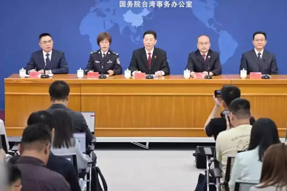 Un grupo de personas sentadas detrás de una mesa en una conferencia de prensa, con un fondo azul que muestra un mapa del mundo y varias personas en la audiencia tomando notas y fotos.