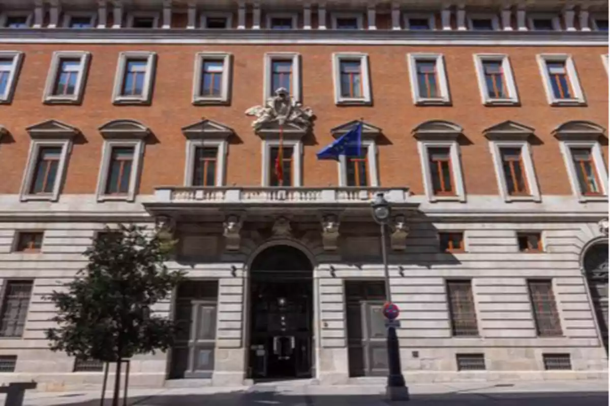 Edificio histórico de ladrillo rojo con ventanas grandes y banderas en la fachada.