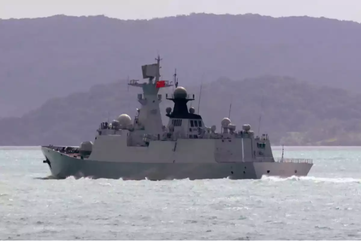 Un buque de guerra navegando en el mar con montañas al fondo.