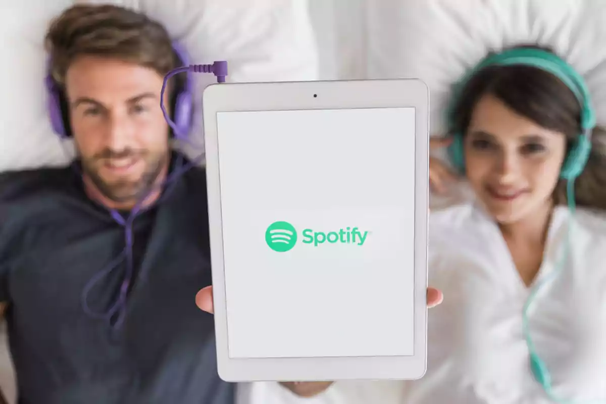 Dos personas acostadas usando audífonos mientras sostienen una tablet con el logo de Spotify en la pantalla.