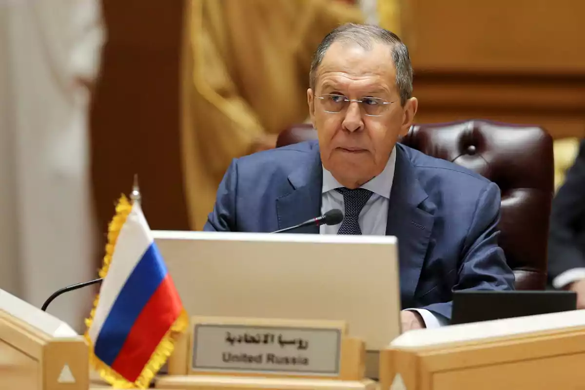 Un hombre en traje sentado en una mesa de conferencias con una bandera de Rusia al frente.