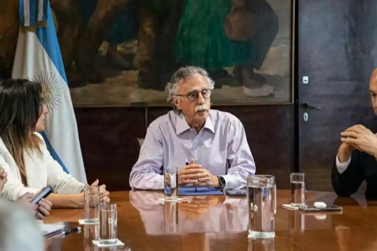 Un grupo de personas sentadas alrededor de una mesa en una reunión con una bandera argentina al fondo.