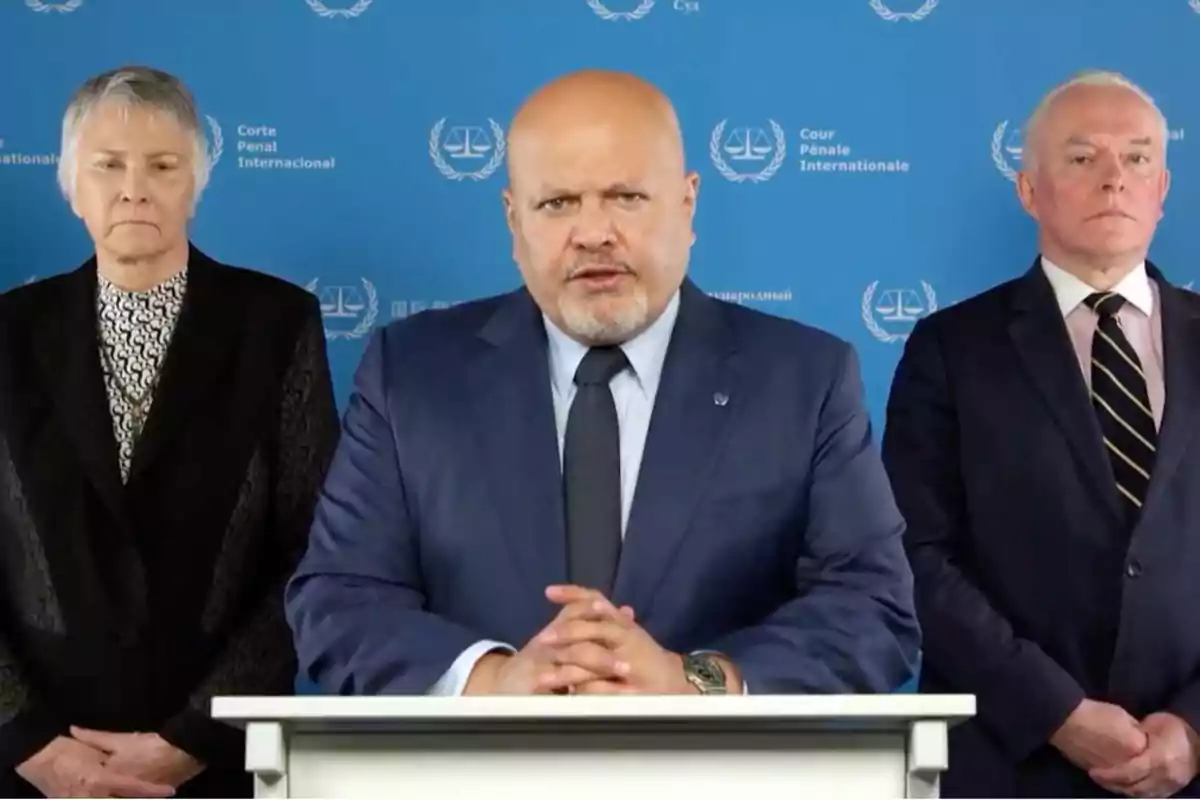 Tres personas de pie frente a un fondo azul con el logo de la Corte Penal Internacional.