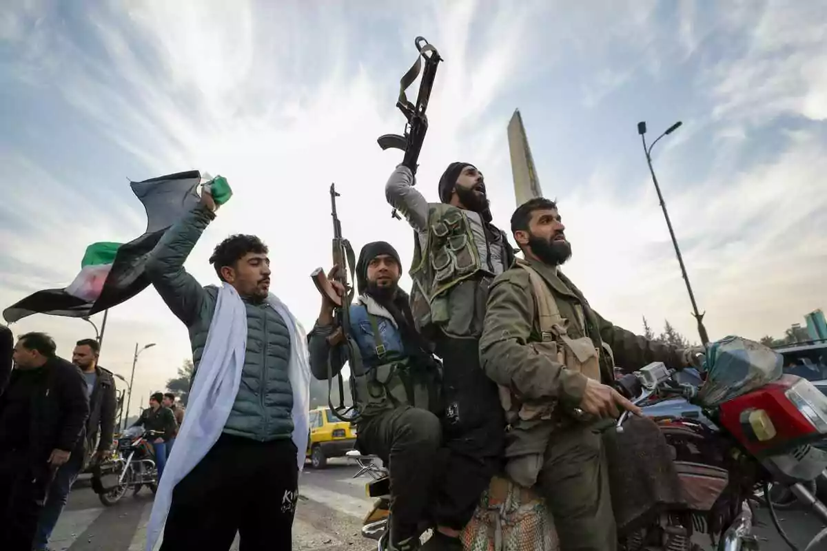 Un grupo de hombres con armas y una bandera se encuentra sobre una motocicleta en una calle concurrida bajo un cielo nublado.