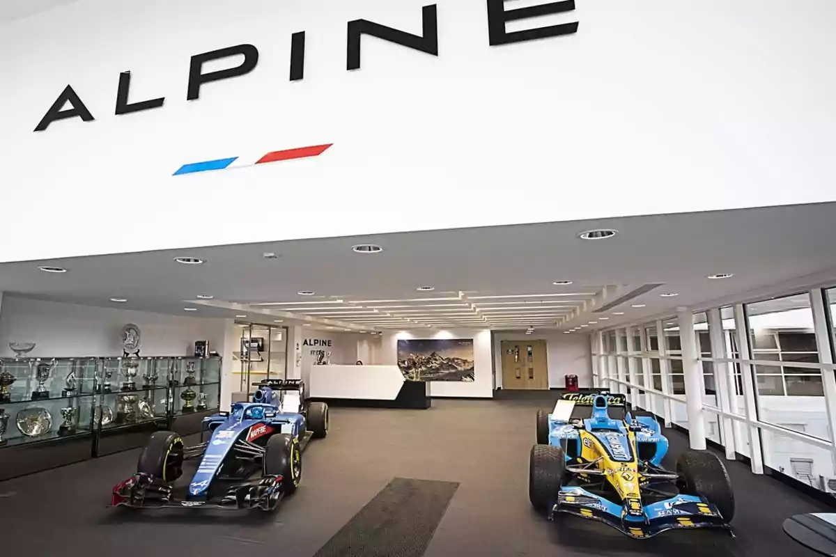 Entrada de una sala de exhibición de Alpine con dos autos de Fórmula 1 y una vitrina de trofeos.