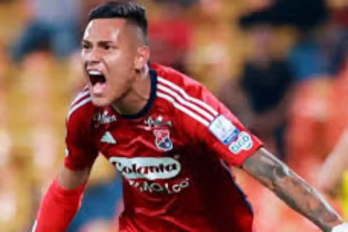 Jugador de fútbol con uniforme rojo celebrando en un estadio.