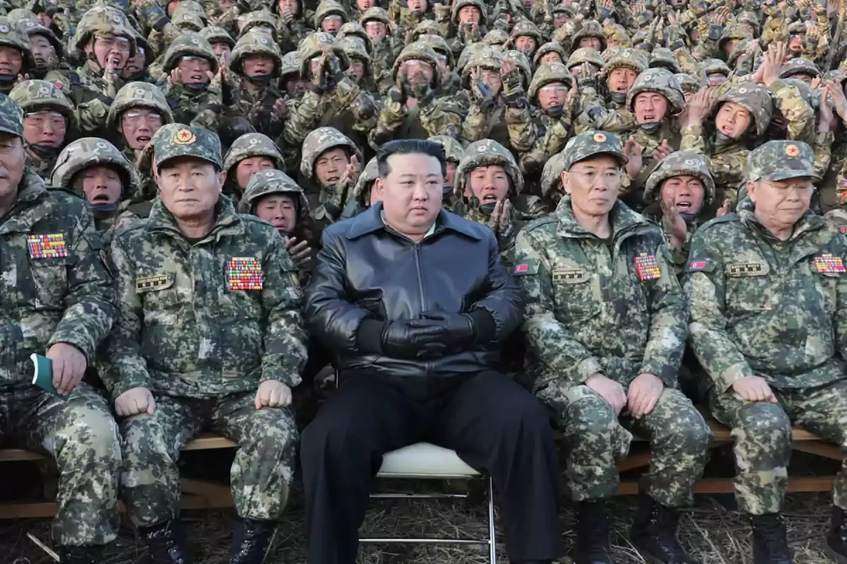 Un grupo de soldados en uniforme militar posando para una foto con un hombre en el centro vestido con una chaqueta negra.