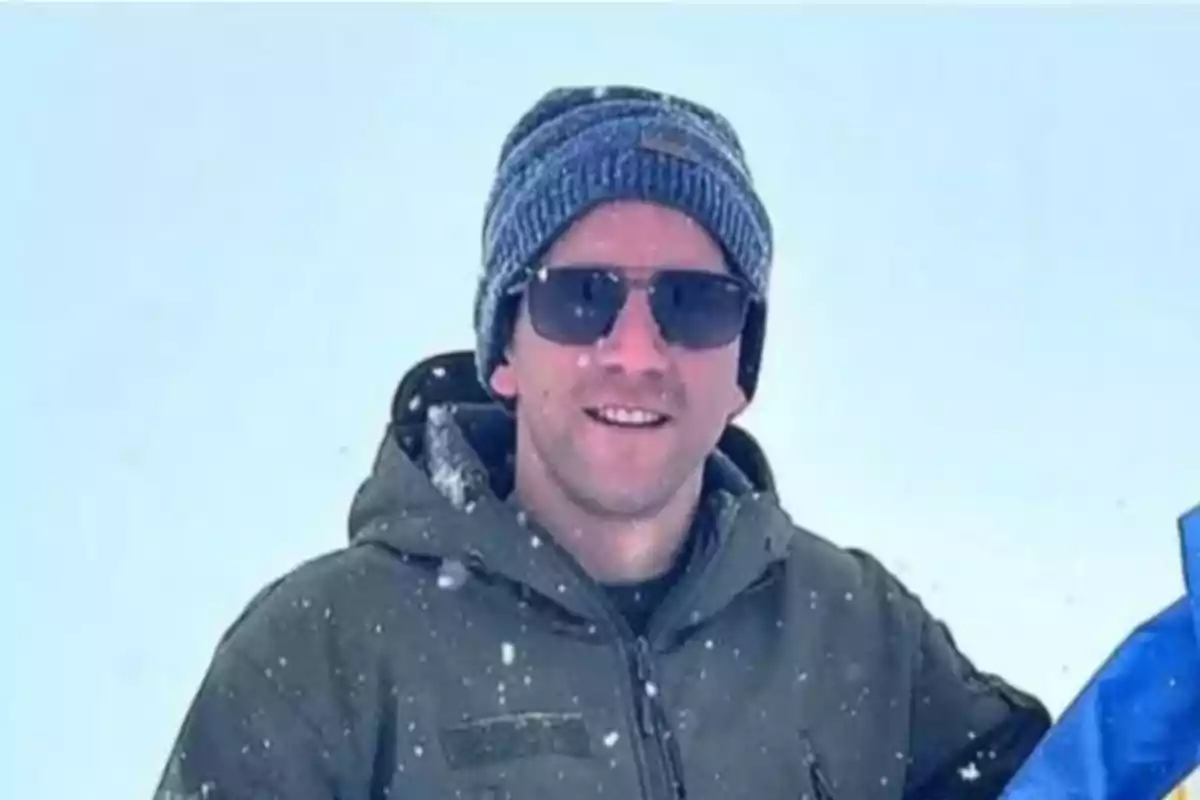 Hombre con gorro y gafas de sol sonriendo en un entorno nevado.